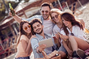 Bira içip beach partide eğleniyor arkadaşlar. Yaz, tatil, tatil, mutluluk ve insanlar kavramı. Selfie tablet ile alarak arkadaş grubu