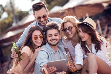 Bira içip beach partide eğleniyor arkadaşlar. Yaz, tatil, tatil, mutluluk ve insanlar kavramı. Selfie tablet ile alarak arkadaş grubu