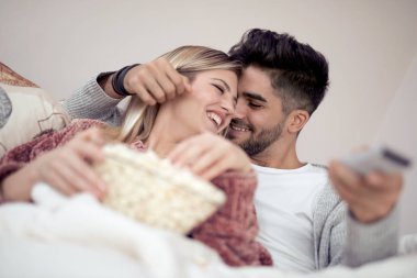 Mutlu genç çift kanepede evde patlamış mısır ile yalan ve Tv izlerken.