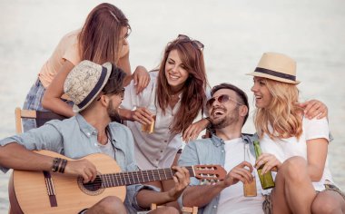 Gençlerin grup birlikte eğleniyor sahilde, gitar çalmak mutlu.