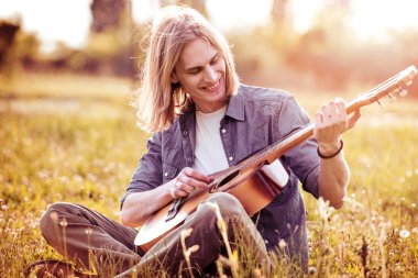 Doğada akustik gitar ile genç modern adam portresi.