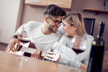 Genç ve güzel bir çift evde dinleniyor ve gitar çalıyor..