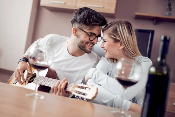 Genç ve güzel bir çift evde dinleniyor ve gitar çalıyor..