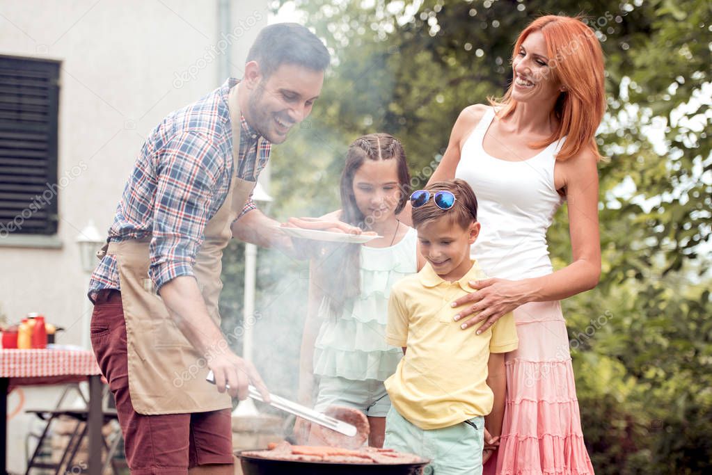 Leisure,food, people and holidays concept-man cooking meat on barbecue grill for his family at summer outdoor party.