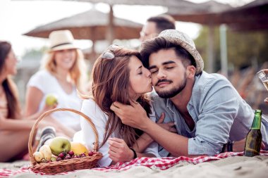 Mutlu genç çift plajda pikniğin tadını çıkarıyor ve yaz tatillerinde iyi vakit geçiriyor..