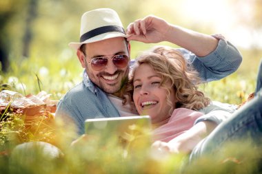 Mutlu genç çift açık havada dinlenirken dijital tablet kullanarak portresi.