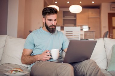 Evde dizüstü bilgisayarda çalışırken içme kahve yakışıklı genç adam.