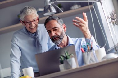 Bir dizüstü bilgisayar kullanarak, söz ve ofiste çalışırken gülümseyen iki olgun iş adamları.