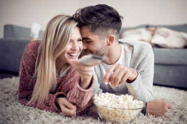 Mutlu genç çift patlamış mısır ile evde yerde yatarken ve Tv izlerken.