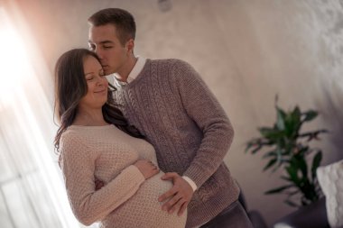 Yakışıklı bir adam ve güzel hamile karısı evlerinin penceresinin yanında durup gülümsüyorlar..