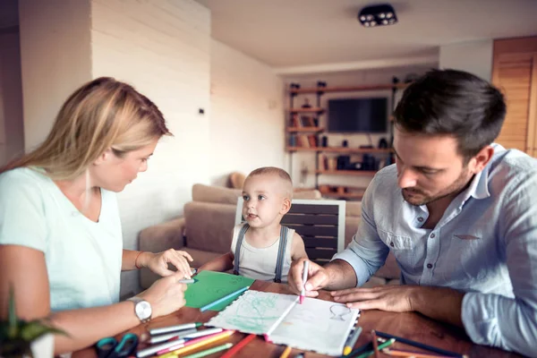 Mom and dad drawing with their son.They are  having fun in their living room.