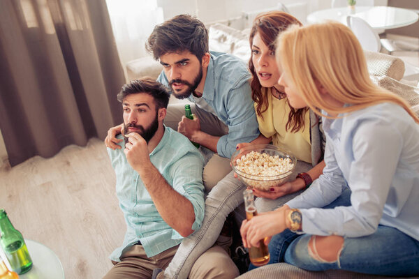 Cheerful group of friends watching football game at home.