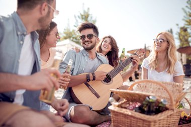 Genç çekici gitar çalmak için arkadaş sahilde otururken adam. Piknik zamanı.