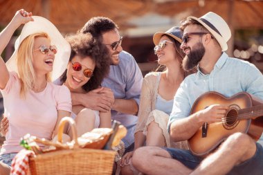 Sahilde, eğleniyor arkadaşlar gitar çalmak.