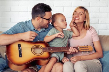 Neşeli Anne, baba ve gitar ile kanepede oturan çocuk