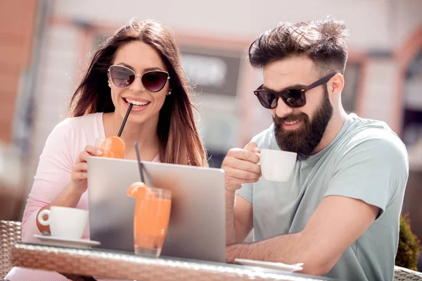 Young couple drinking coffee in cafe. They are smiling and looking at laptop.