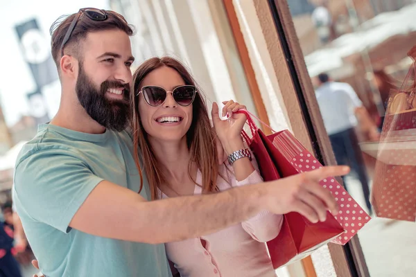 若いカップルが店の窓を見て買い物袋 — ストック写真