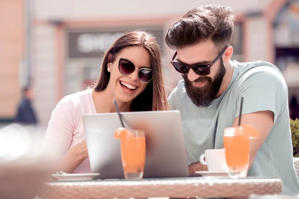 若いカップルがカフェでコーヒーを飲みます 笑みを浮かべて ノート パソコンを見ていると楽しい時を過す — ストック写真