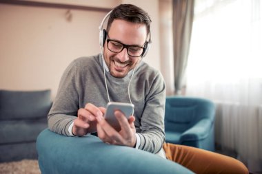 Kulaklıklar giyen ve evde akıllı telefonuna müzik dinlemek genç adam.