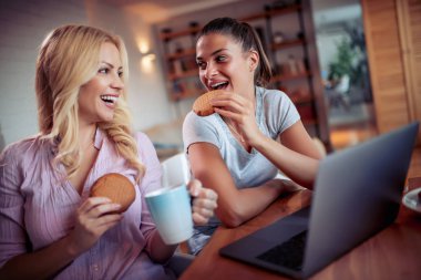 Dizüstü bilgisayar kullanarak ve yemek iki mutlu kız 