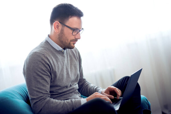 Young man working with laptop on armchair at home office.