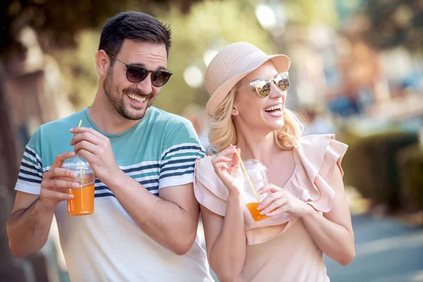 beautiful young couple drinking orange juice and laughing in park in daylight