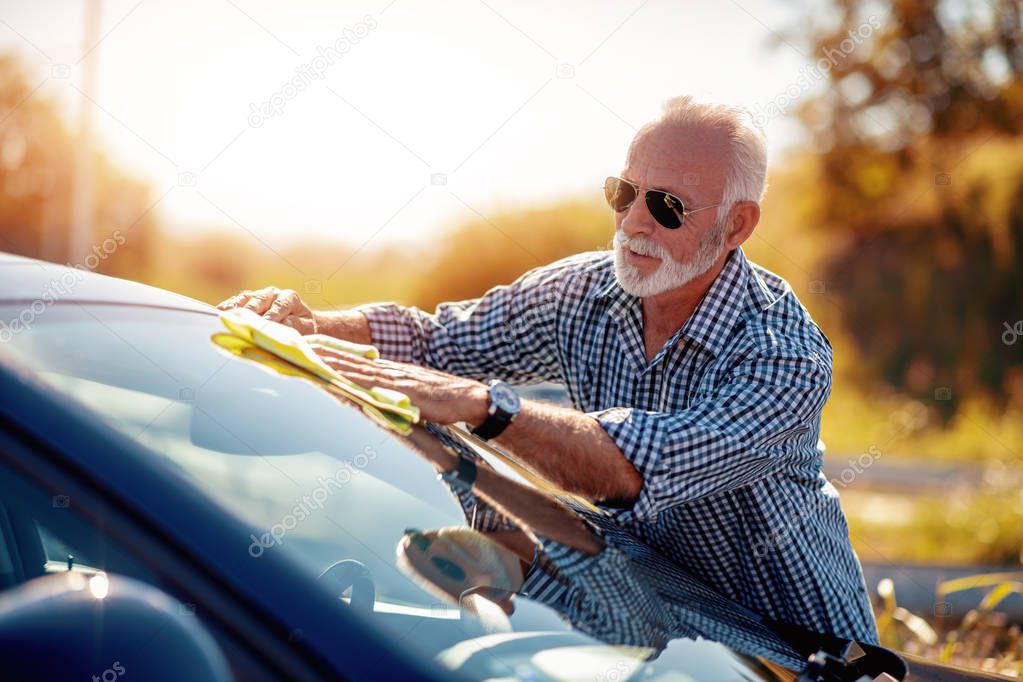Senior man cleaning car on open air