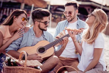 Grup arkadaşıyla pizza yiyip bira içmeyi süre sahilde, gitar çalmak, piknik çekici.