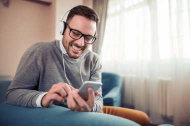 Kulaklıklar giyen ve evde akıllı telefonuna müzik dinlemek genç adam.