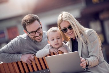 Anne ve küçük çocuk şehir parkta otururken dizüstü bilgisayar kullanarak