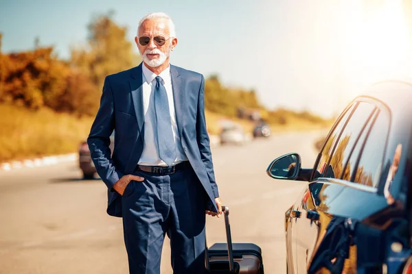 Traveling businessman with luggage near car