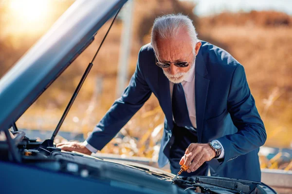 Senior businessman trying fix broken car by roadside