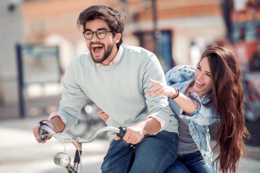 Mutlu çift için bir bisiklet mi şehirde güneşli bir günde binmek. Kız bir şey parmağıyla gösterir.