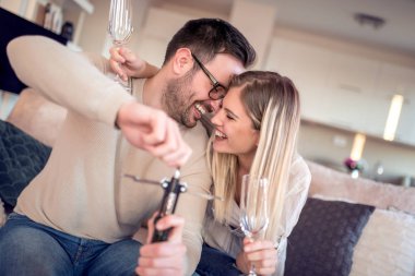 Oturma odasında kanepede oturan genç romantik çift şarap içip aşık keyfini çıkarın.