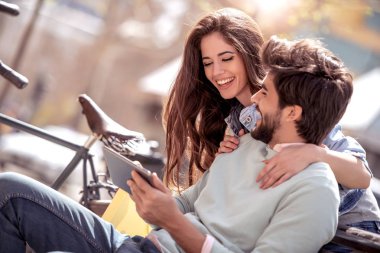 Genç çift, park bankında oturan ve tablet ile eğleniyor. Aşk, insanlar, eğlenceli ve mutluluk kavramı.