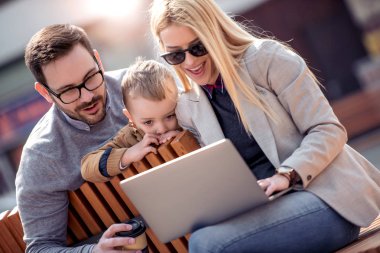 Mutlu bir aile ve dijital teknoloji. Anne ve küçük çocuk şehir parkta otururken dizüstü bilgisayar kullanarak.