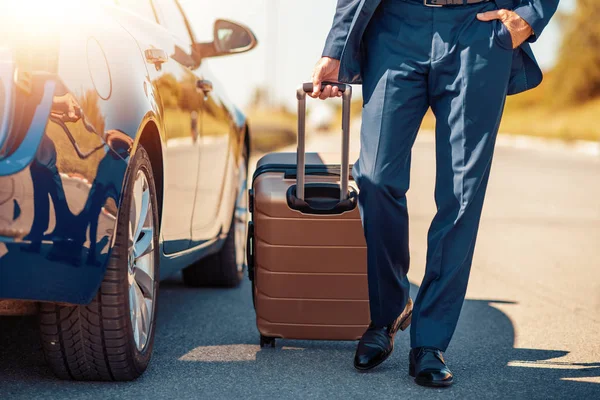 Traveling businessman with his luggage near car.