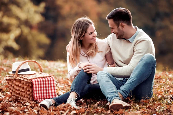 Couple in love sitting on autumn leaves in a park, enjoying a beautiful autumn day.