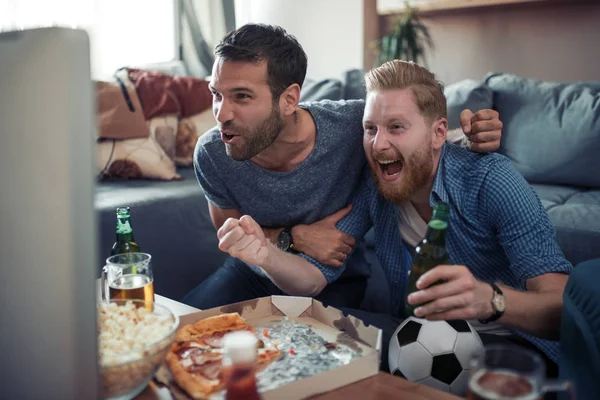 Friendship, sport, people and entertainment concept- football fans watching soccer on tv at home.