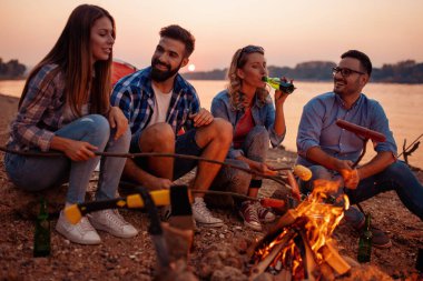 Rahatlatıcı ve yaz akşamında kumsalda zevk mutlu genç arkadaş grubu.