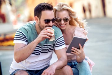 Kahve içme ve yaz aylarında şehir parkında oturan ve tablet bilgisayarı kullanan genç çift.