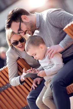 Mutlu baba, anne ve oğul şehrin bankta otururken dijital tablet kullanma.