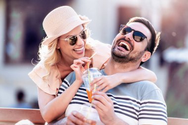 Bankta oturup meyve suyu içen gülümseyen çiftin portresi..