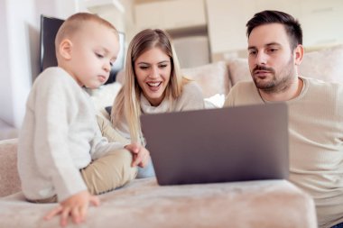 Birlikte eğleniyor, neşeli genç bir aile portresi. Oturma odasında dizüstü bilgisayar kullanarak.