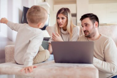 Birlikte eğleniyor, neşeli genç bir aile portresi. Oturma odasında dizüstü bilgisayar kullanarak.