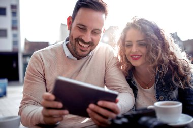 Kafede tablet ile genç çift. Gülmek ve kahve içerler.