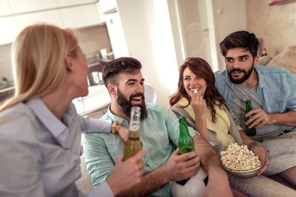Friends watching football game on tv,drink beer, eat  popcorn and having great time together.