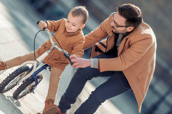 Father learn his little son to ride a bicycle, having fun together.