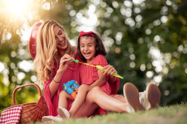 Anne ve küçük kızı eğleniyor, sabun köpüğü birlikte parkta üfleme.