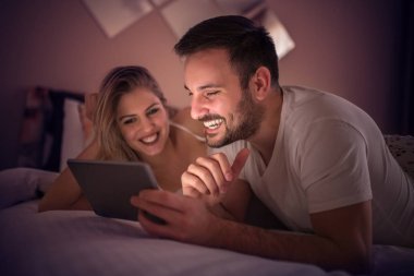 Genç çift otel odasında geceleri yatakta yatıyordu süre tablet kullanma.